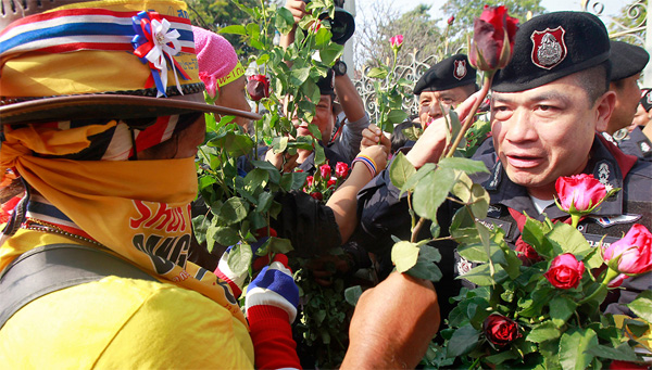 A protester gives red roses to a Thai policeman at the Government house in BangkokReuters